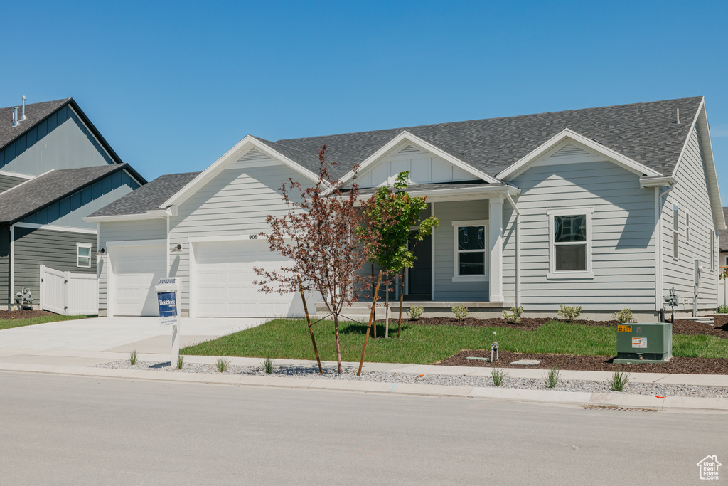 View of front facade featuring an attached garage, driveway, roof with shingles, covered porch, and a front yard