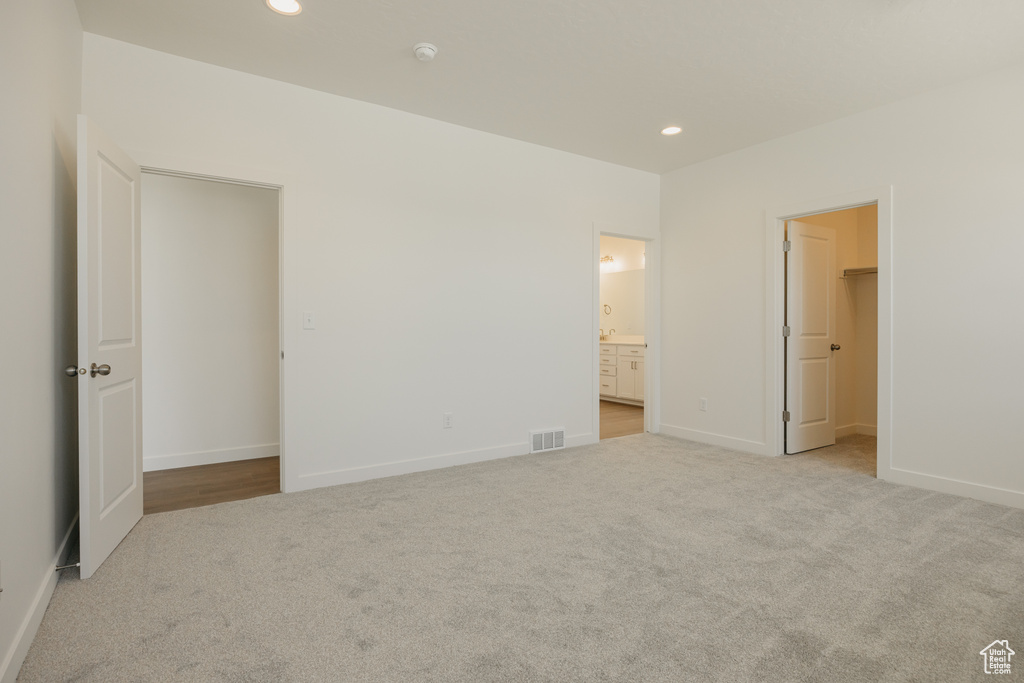 Unfurnished bedroom with carpet, a walk in closet, recessed lighting, baseboards, and ensuite bathroom