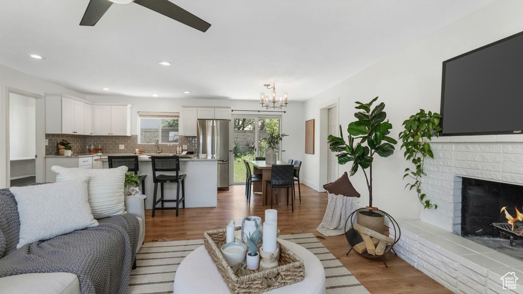 Living area with a chandelier, ceiling fan, wood finished floors, a brick fireplace, and recessed lighting