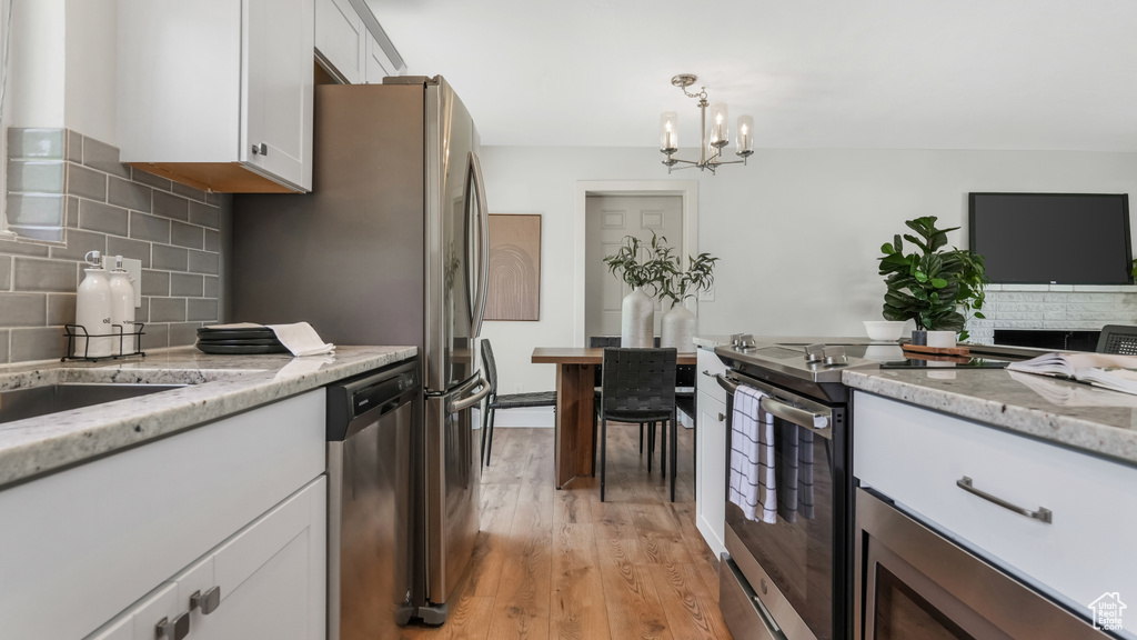 Kitchen featuring stainless steel appliances, light wood-style floors, a chandelier, decorative backsplash, and white cabinetry