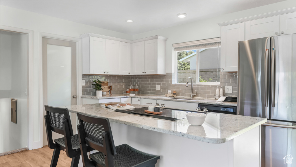 Kitchen featuring freestanding refrigerator, a kitchen breakfast bar, white cabinets, backsplash, and light wood finished floors