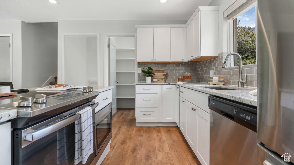 Kitchen featuring appliances with stainless steel finishes, a sink, white cabinets, tasteful backsplash, and light stone counters