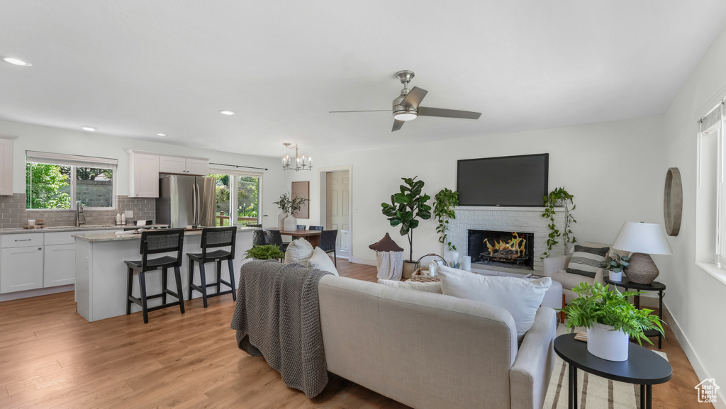 Living area with a fireplace, a ceiling fan, light wood-style floors, recessed lighting, and a chandelier