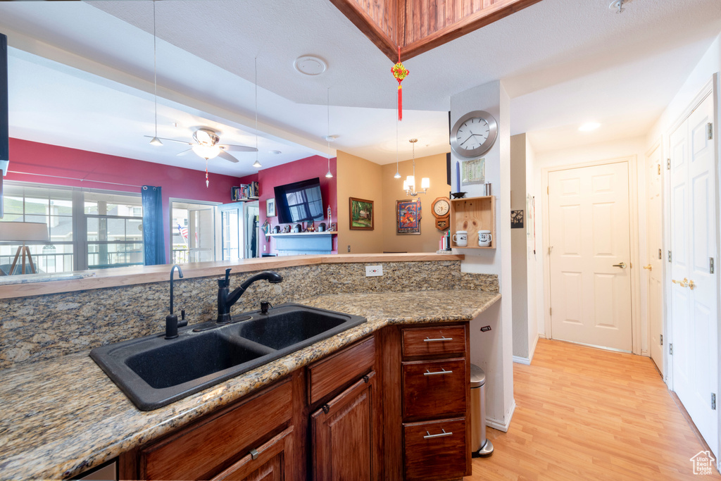 Kitchen with a sink, light wood-type flooring, a ceiling fan, pendant lighting, and light stone countertops