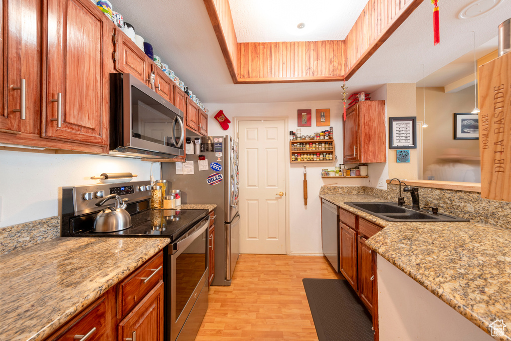 Kitchen featuring appliances with stainless steel finishes, a sink, light wood-style flooring, a raised ceiling, and light stone counters