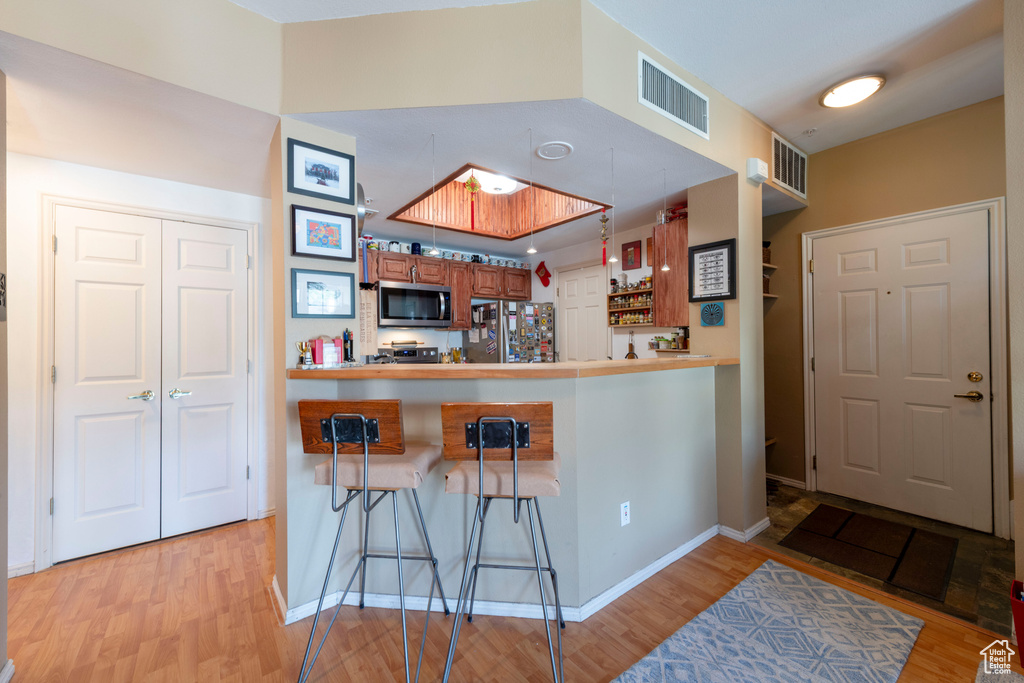 Kitchen with appliances with stainless steel finishes, brown cabinets, light wood-type flooring, a kitchen breakfast bar, and baseboards
