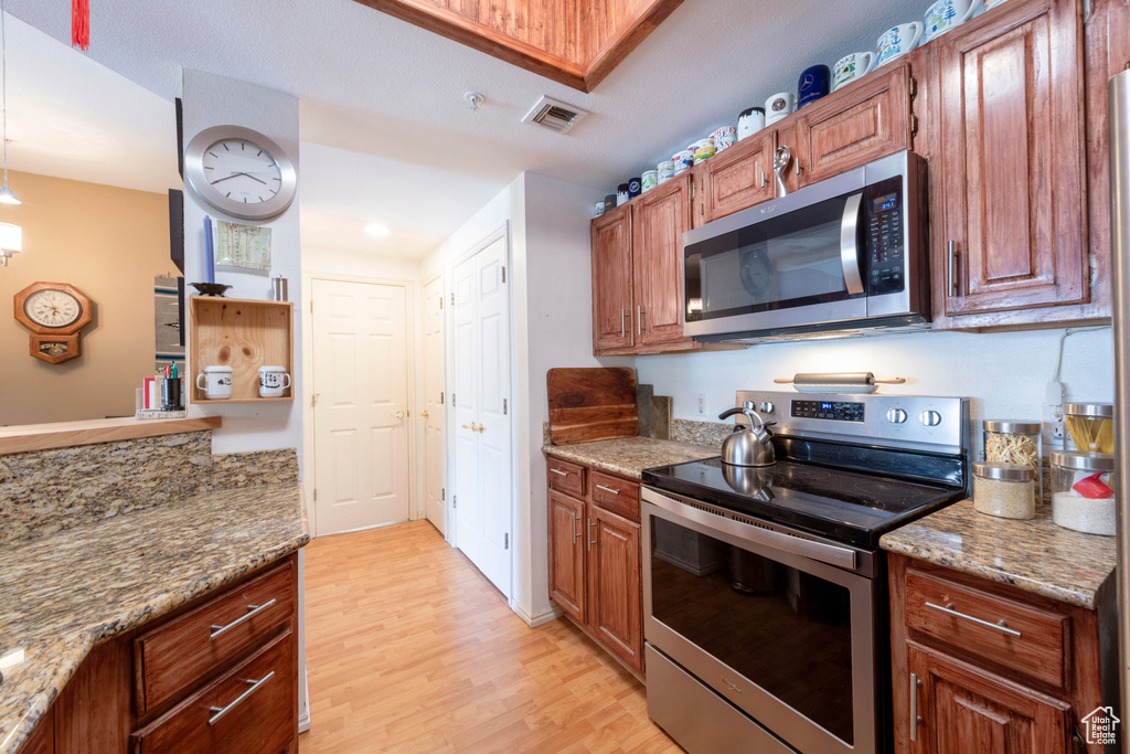 Kitchen with stainless steel appliances, light wood-style floors, light stone counters, brown cabinets, and recessed lighting