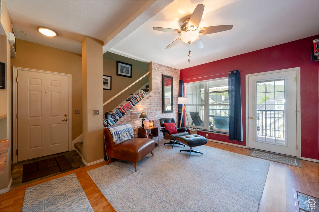 Living area with wood finished floors, stairway, a ceiling fan, brick wall, and an accent wall