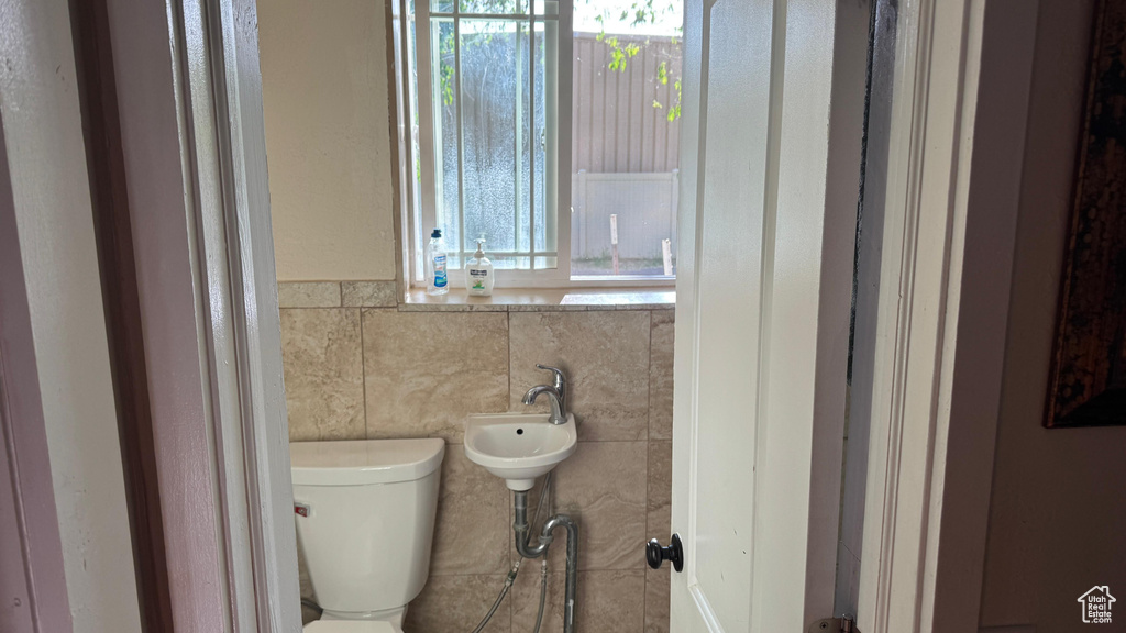 Bathroom featuring healthy amount of natural light, toilet, and tile walls