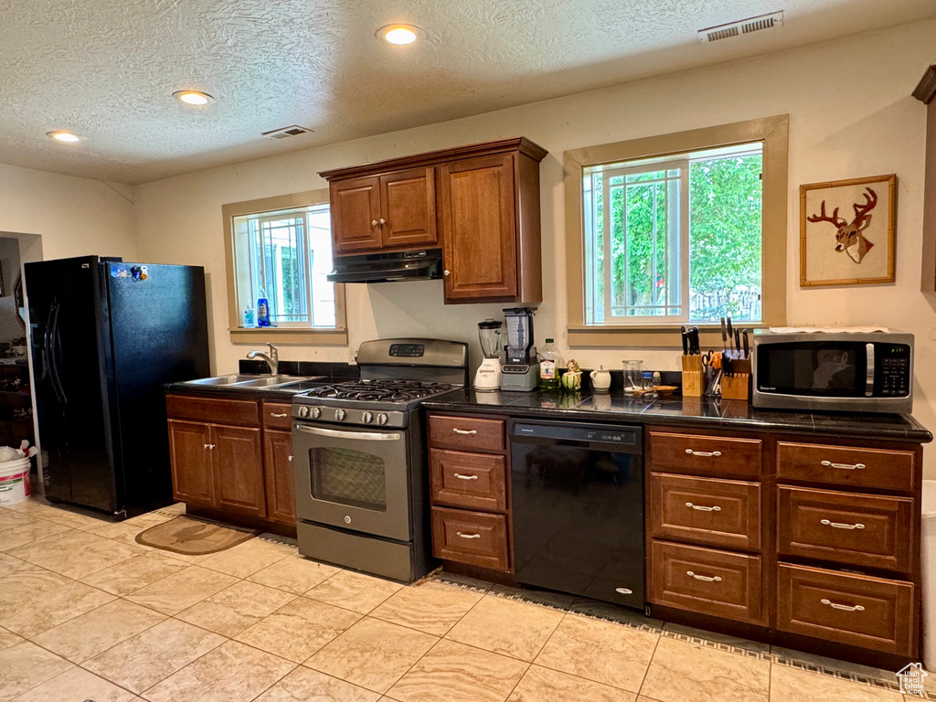 Kitchen with black appliances, under cabinet range hood, dark countertops, a textured ceiling, and a sink
