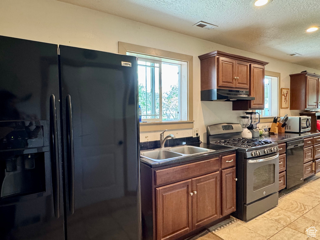 Kitchen with black appliances, a sink, dark countertops, under cabinet range hood, and a textured ceiling