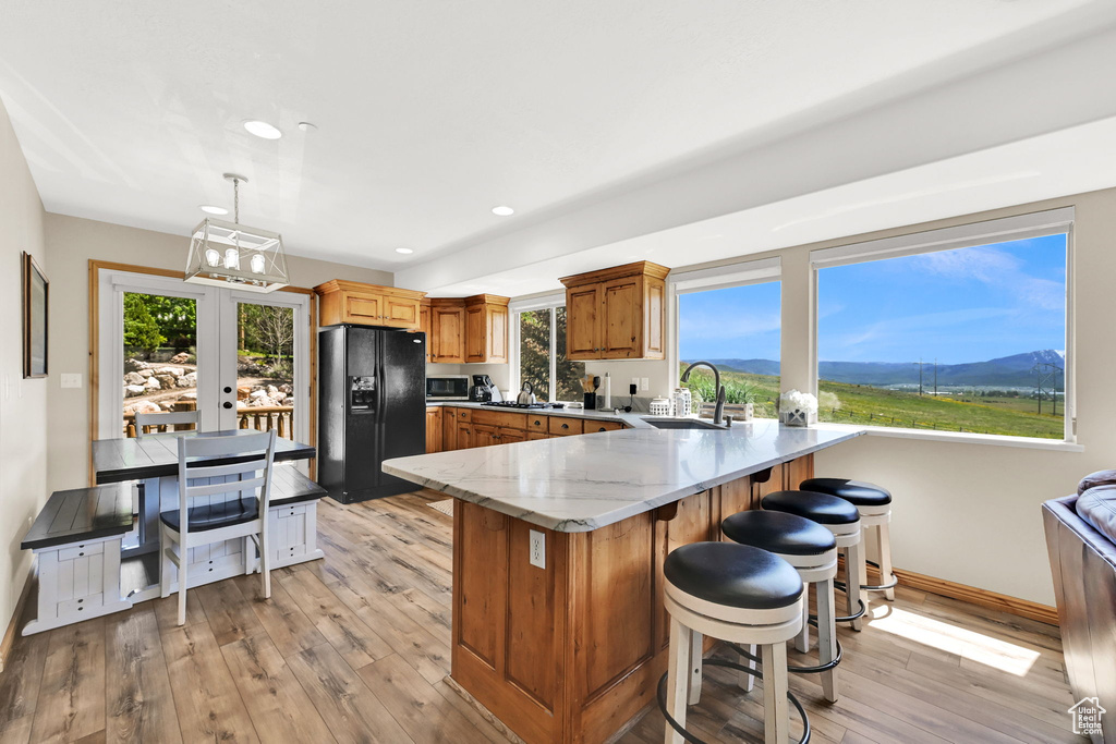 Kitchen featuring black fridge with ice dispenser, a sink, stainless steel microwave, a peninsula, and light wood finished floors