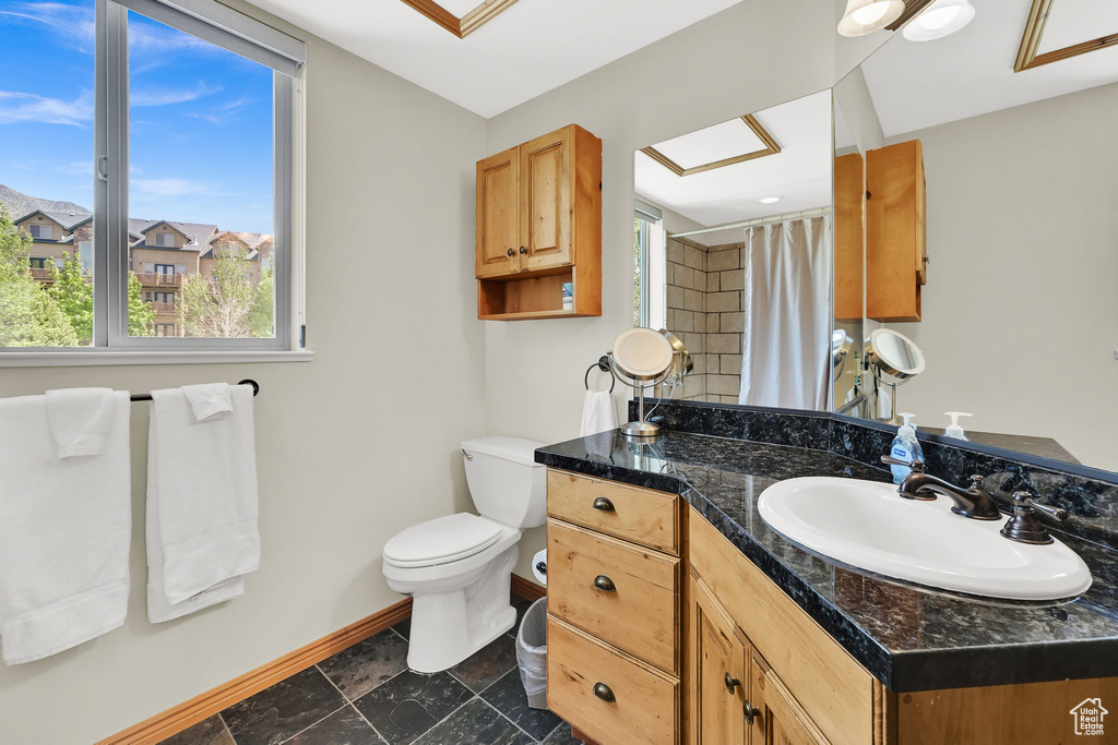 Full bathroom with baseboards, vanity, toilet, and plenty of natural light