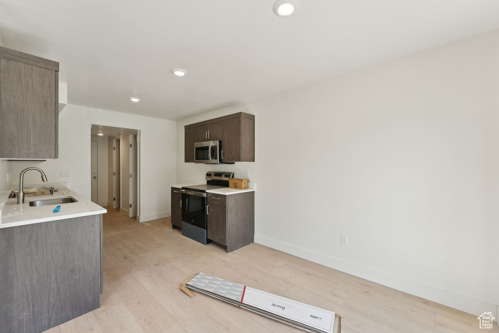 Kitchen with stainless steel appliances, a sink, light wood-style flooring, light countertops, and recessed lighting