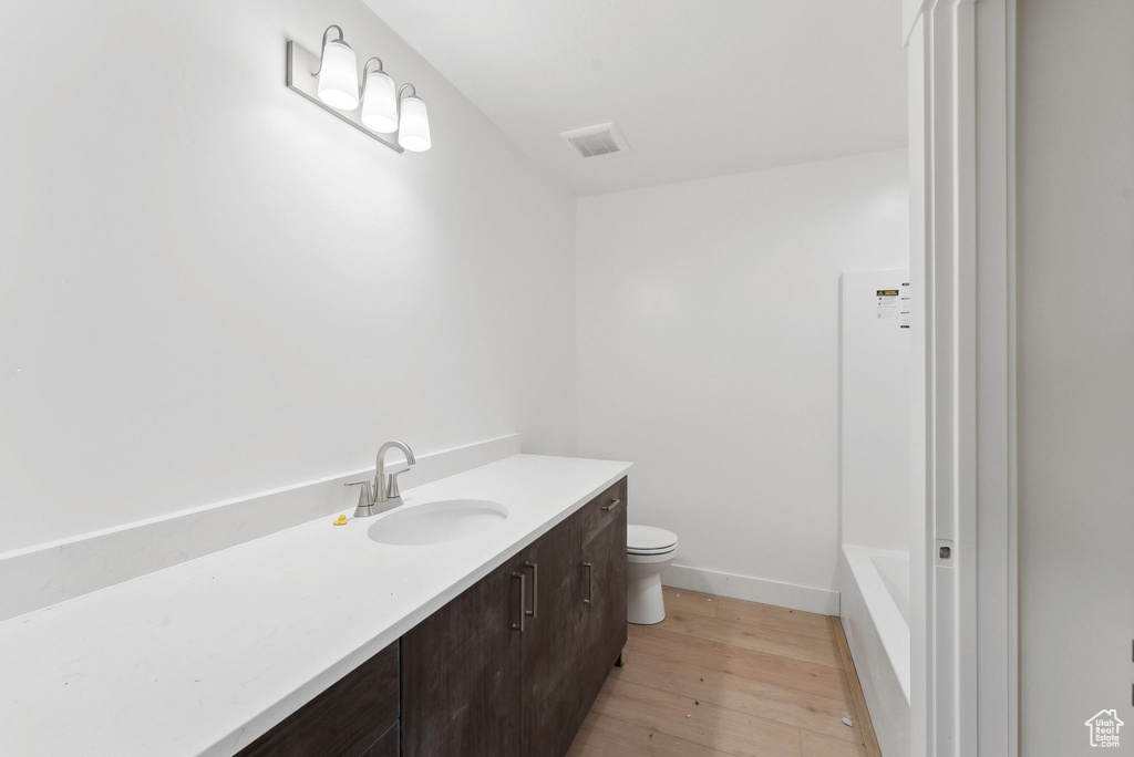 Bathroom with toilet, wood finished floors, vanity, a bathtub, and baseboards