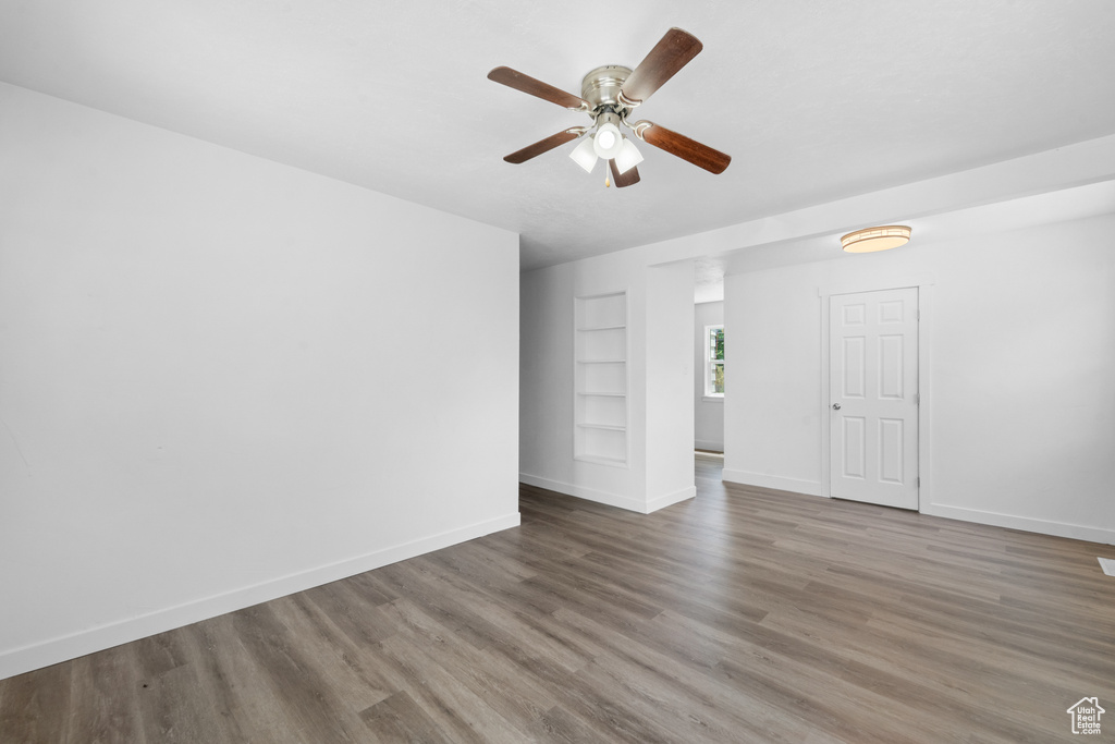 Empty room featuring built in features, a ceiling fan, and wood finished floors