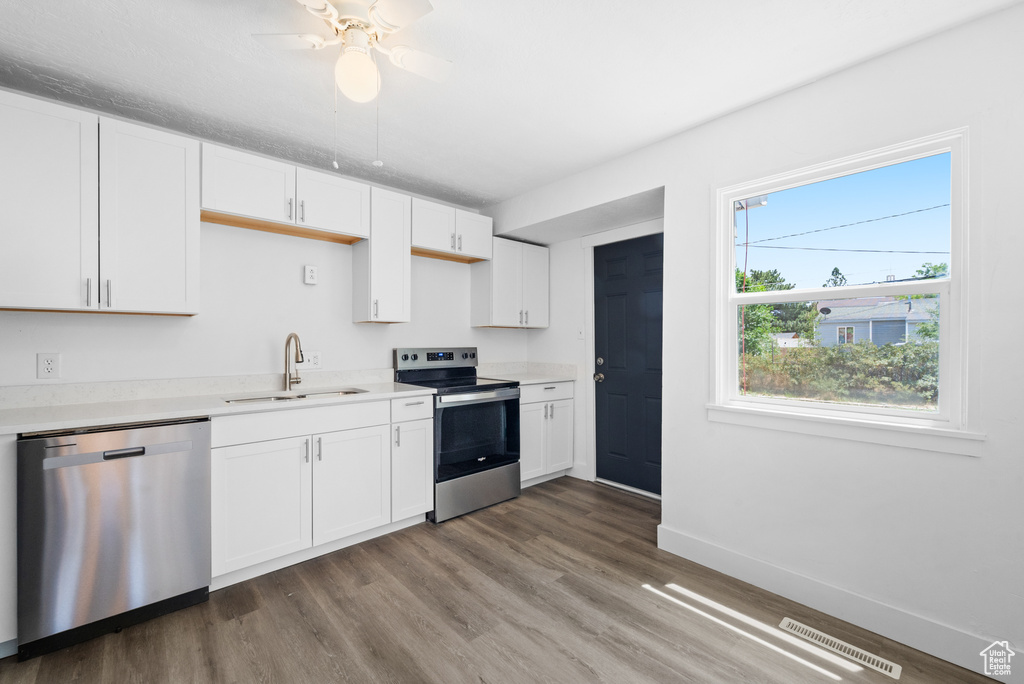 Kitchen with appliances with stainless steel finishes, wood finished floors, white cabinetry, light countertops, and ceiling fan