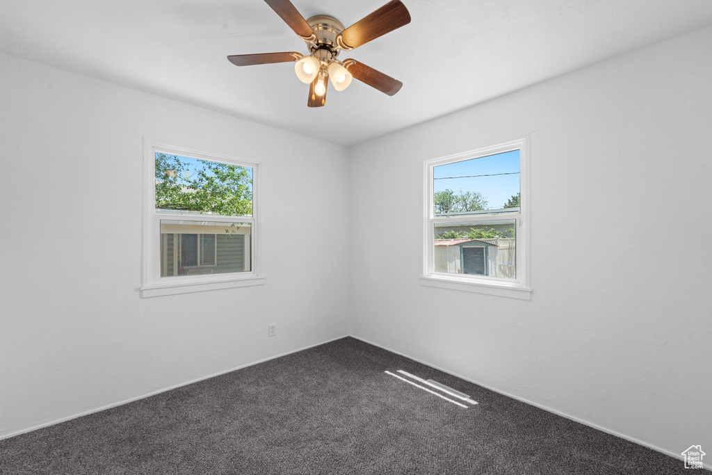 Spare room with healthy amount of natural light, dark carpet, and a ceiling fan