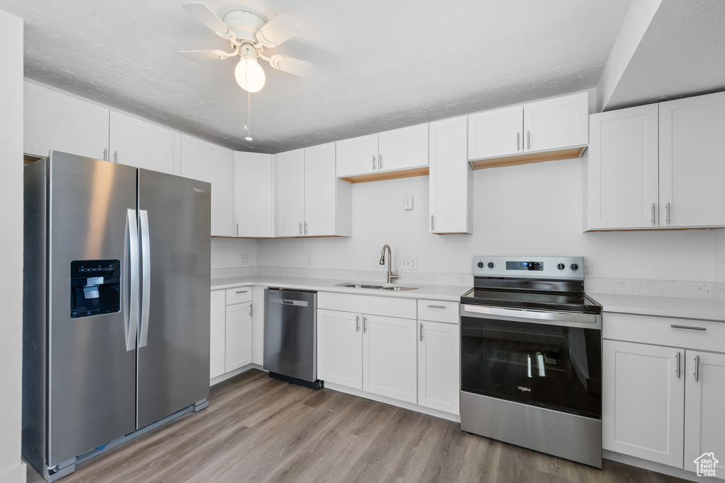 Kitchen with appliances with stainless steel finishes, light wood-style flooring, light countertops, and white cabinets