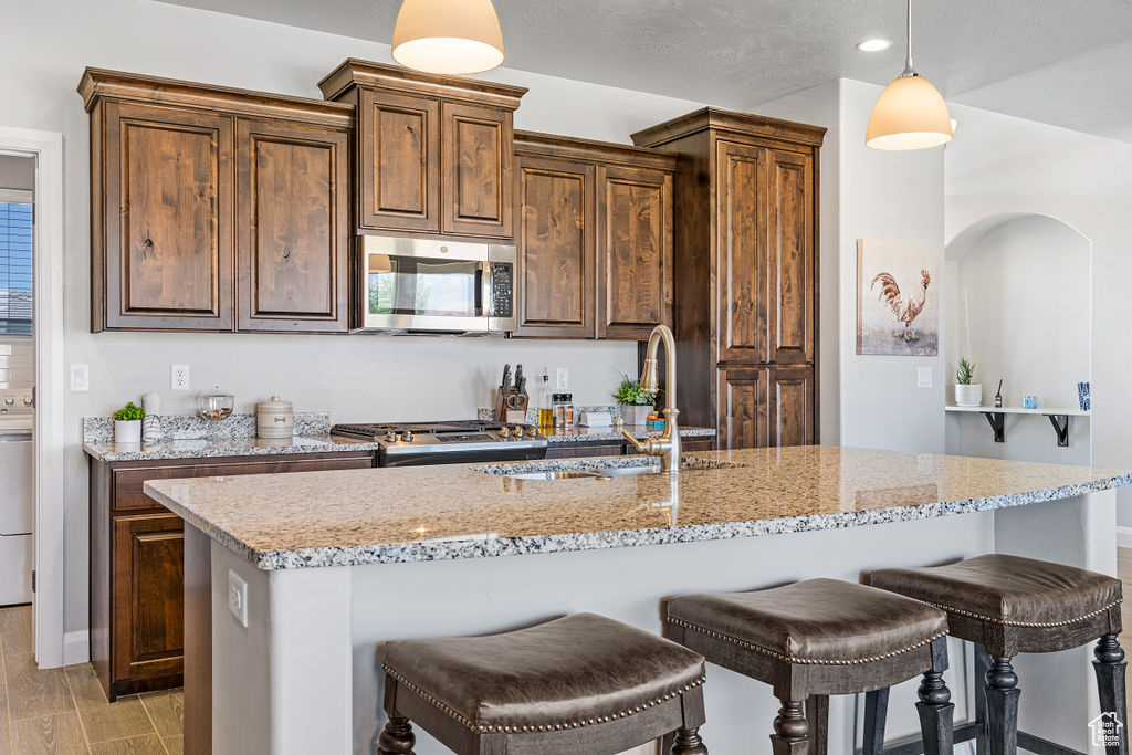 Kitchen featuring stainless steel microwave, a sink, a kitchen bar, light stone countertops, and pendant lighting