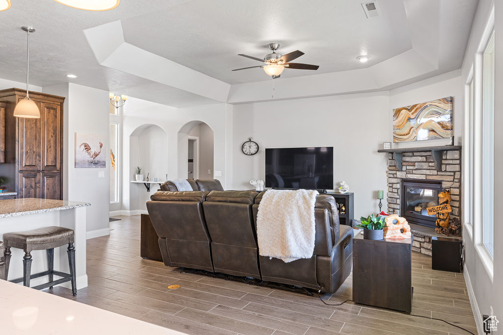 Living area with a ceiling fan, wood finish floors, arched walkways, and a raised ceiling