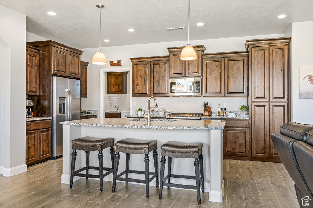 Kitchen with stainless steel appliances, light wood-style floors, a sink, a breakfast bar, and an island with sink