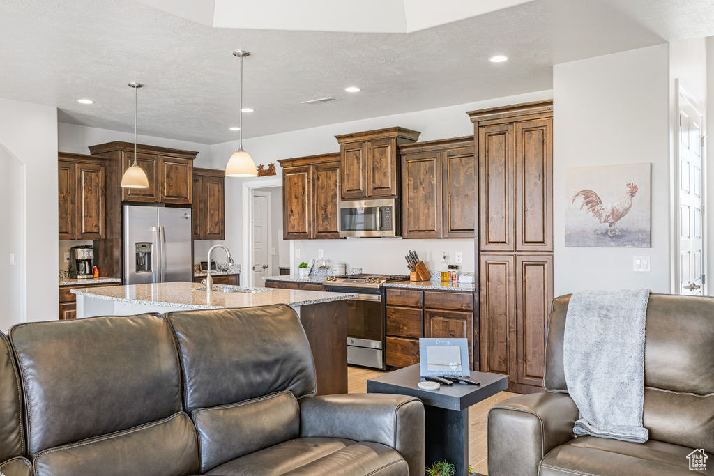 Kitchen with stainless steel appliances, a sink, open floor plan, recessed lighting, and light stone countertops