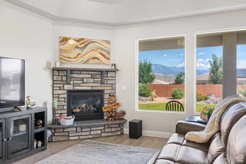 Living room featuring wood finished floors, a mountain view, a stone fireplace, and baseboards