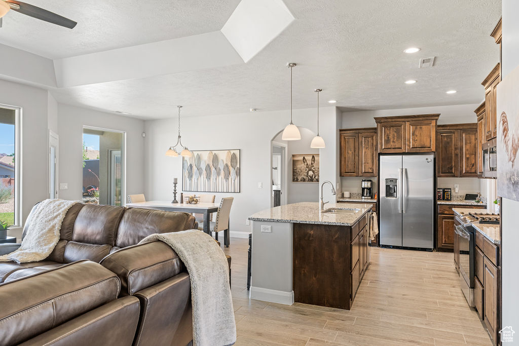 Kitchen featuring appliances with stainless steel finishes, open floor plan, a sink, ceiling fan, and light wood-type flooring