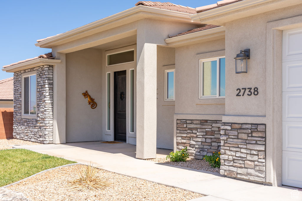 Doorway to property featuring stone siding, stucco siding, and a tile roof