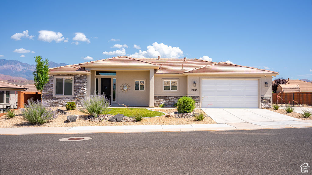 Prairie-style house with stone siding, stucco siding, a tiled roof, and an attached garage