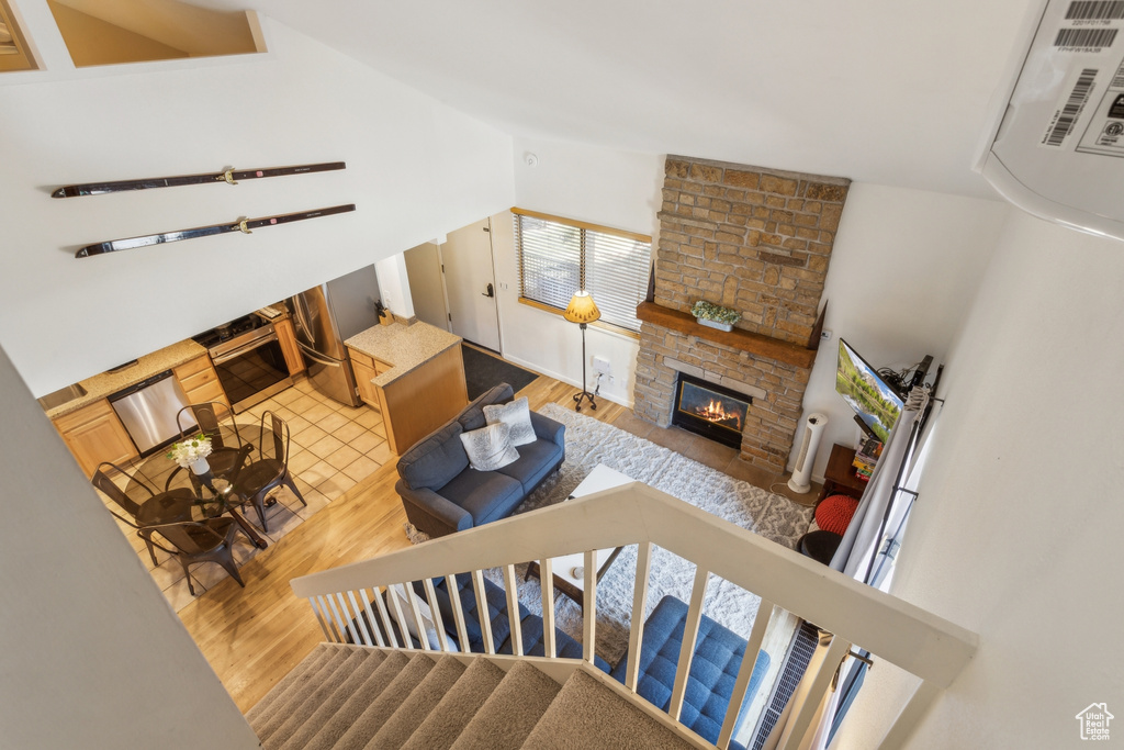 Living area with light wood-style floors, lofted ceiling, a stone fireplace, and stairway