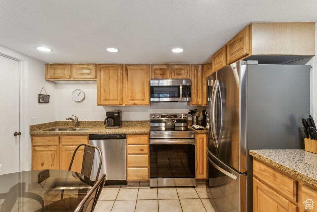 Kitchen with appliances with stainless steel finishes, light stone counters, a sink, recessed lighting, and light tile patterned flooring