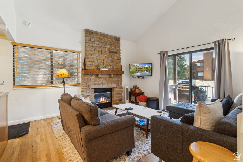 Living room with high vaulted ceiling, wood finished floors, a stone fireplace, and baseboards