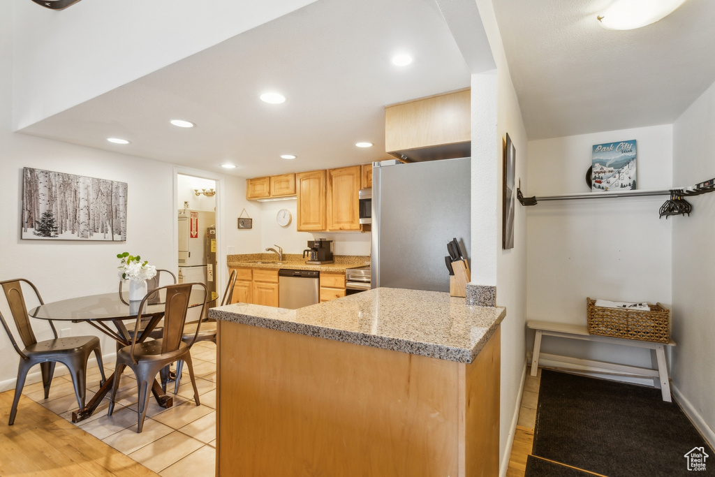 Kitchen featuring appliances with stainless steel finishes, light brown cabinetry, a sink, recessed lighting, and a peninsula