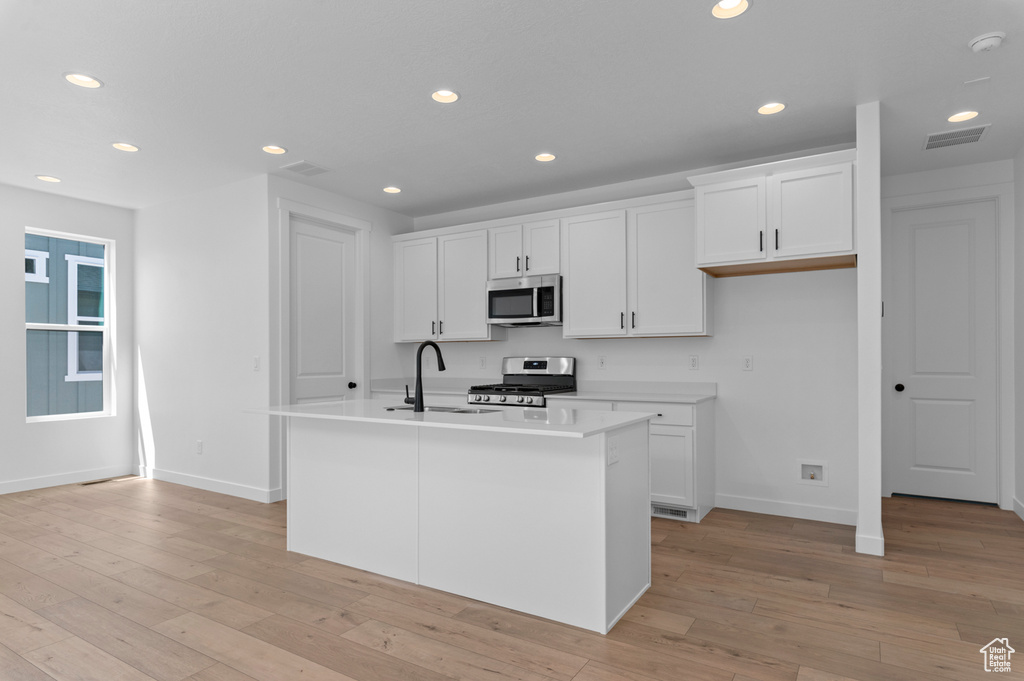 Kitchen with appliances with stainless steel finishes, a sink, baseboards, white cabinets, and recessed lighting