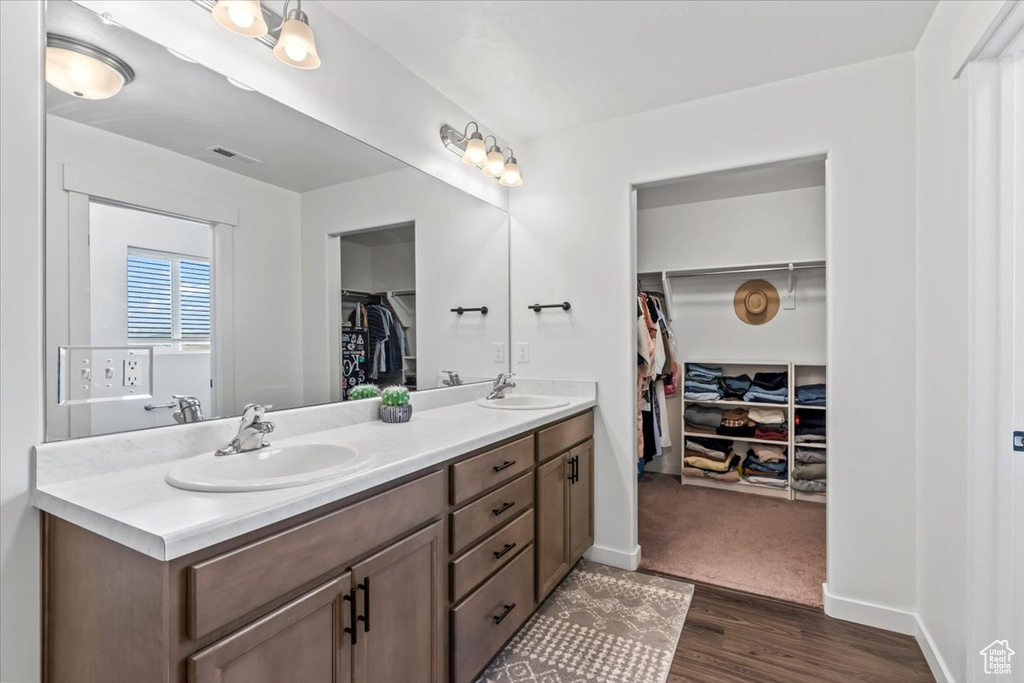 Bathroom with double vanity, a spacious closet, wood finished floors, and baseboards
