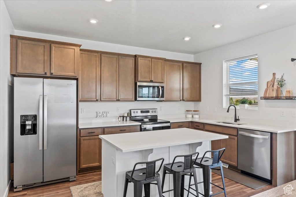 Kitchen with appliances with stainless steel finishes, a sink, wood finished floors, a breakfast bar, and recessed lighting