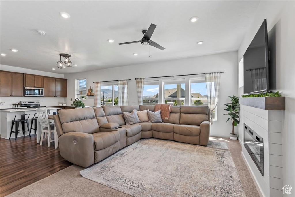 Carpeted living area with recessed lighting, plenty of natural light, ceiling fan, a glass covered fireplace, and a chandelier