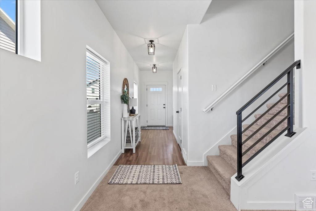 Carpeted foyer entrance with stairs, baseboards, and wood finished floors