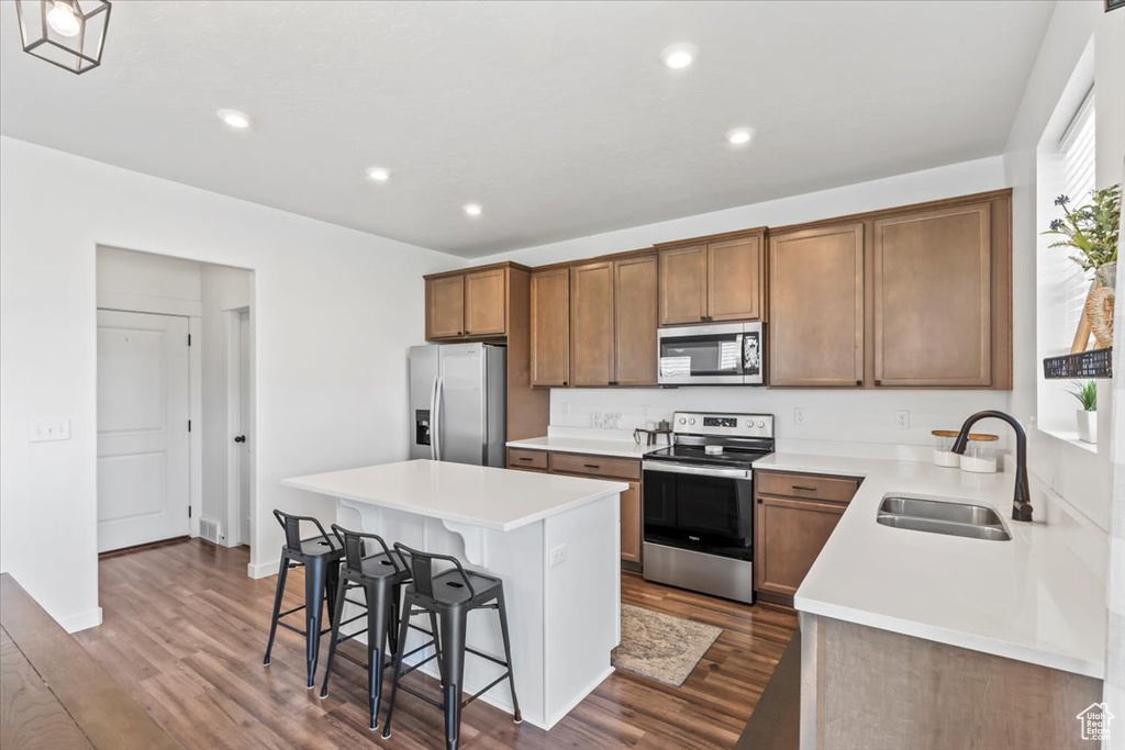 Kitchen with appliances with stainless steel finishes, a sink, a kitchen breakfast bar, a center island, and dark wood-style flooring
