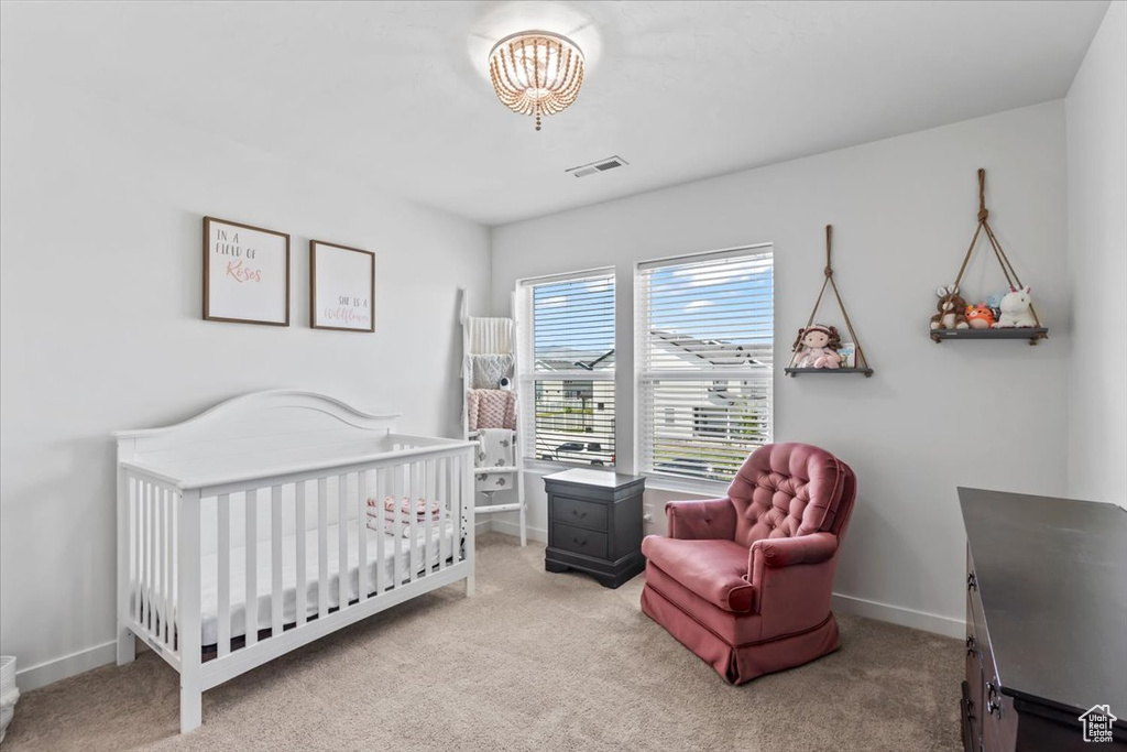 Carpeted bedroom featuring baseboards, a nursery area, and a chandelier
