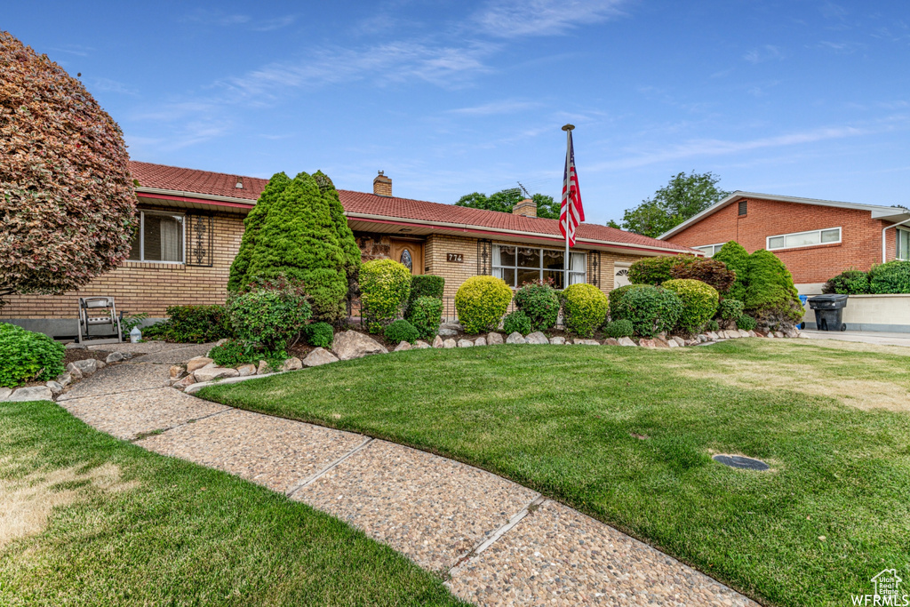 Single story home with a chimney, brick siding, a front lawn, and a tile roof