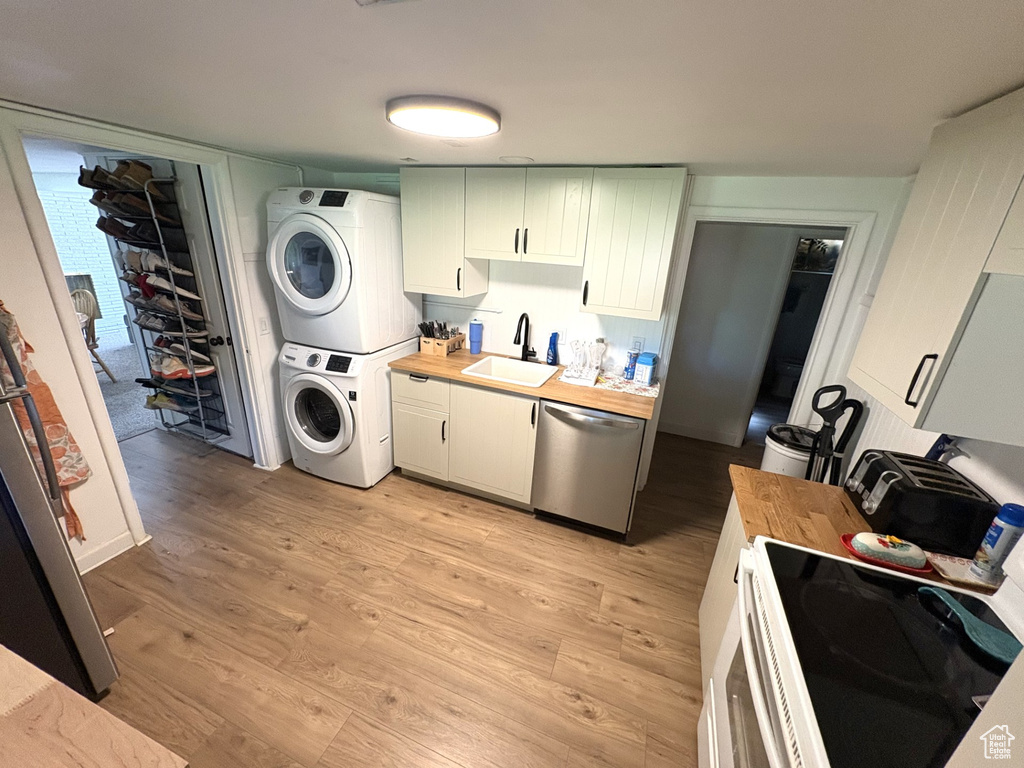 Kitchen with stacked washing machine and dryer, stainless steel dishwasher, a sink, butcher block countertops, and light wood-style flooring