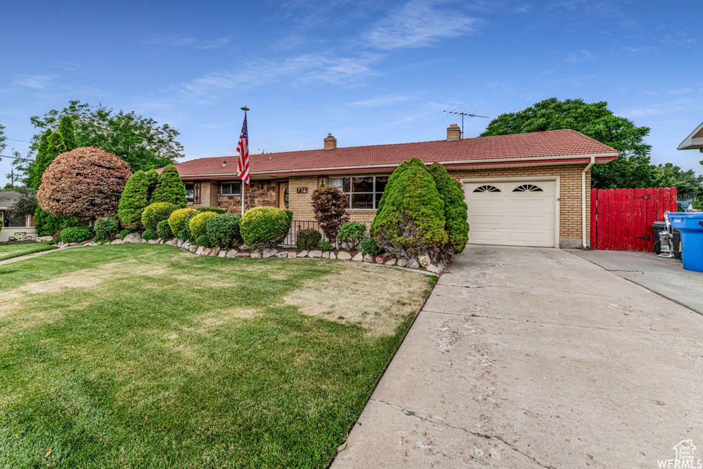 Ranch-style home with concrete driveway, an attached garage, brick siding, a chimney, and a tiled roof