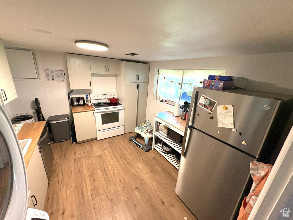 Kitchen featuring freestanding refrigerator, electric range, light wood-style flooring, light countertops, and white cabinetry