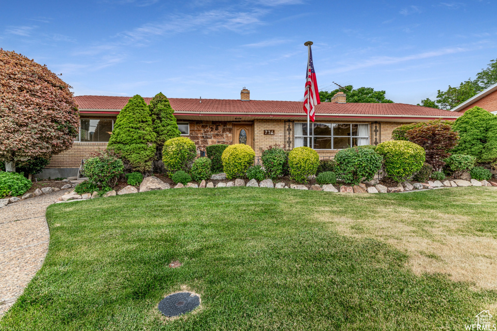 Ranch-style house featuring brick siding, a tile roof, and a front lawn