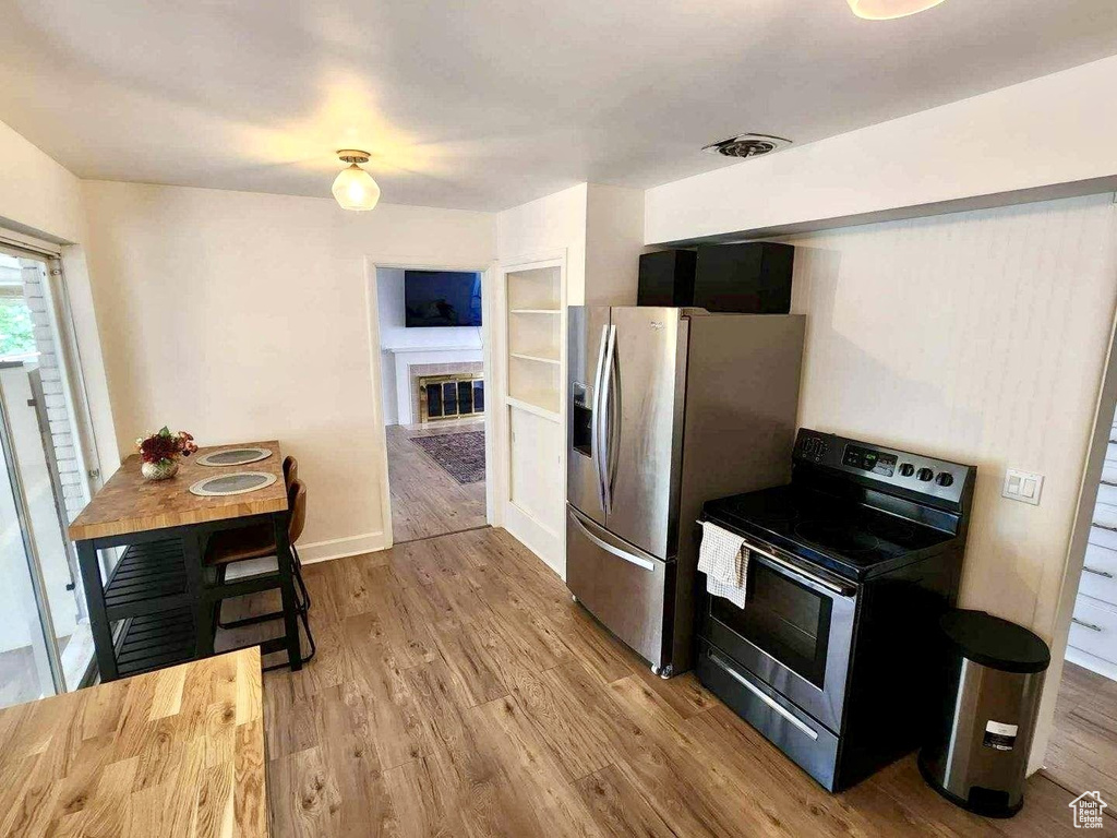 Kitchen featuring appliances with stainless steel finishes, a glass covered fireplace, wood finished floors, and baseboards