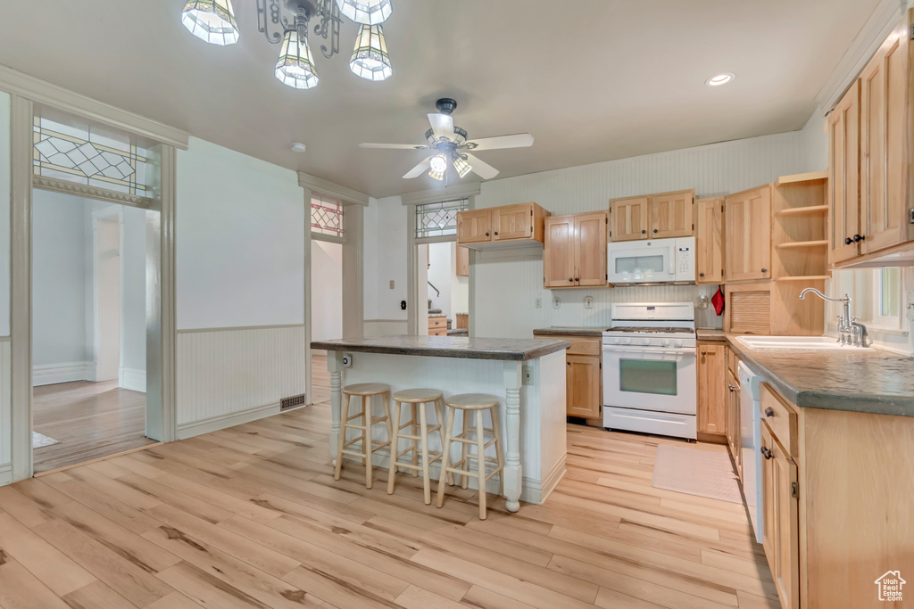 Kitchen featuring white appliances, a sink, light brown cabinets, light wood finished floors, and a wainscoted wall