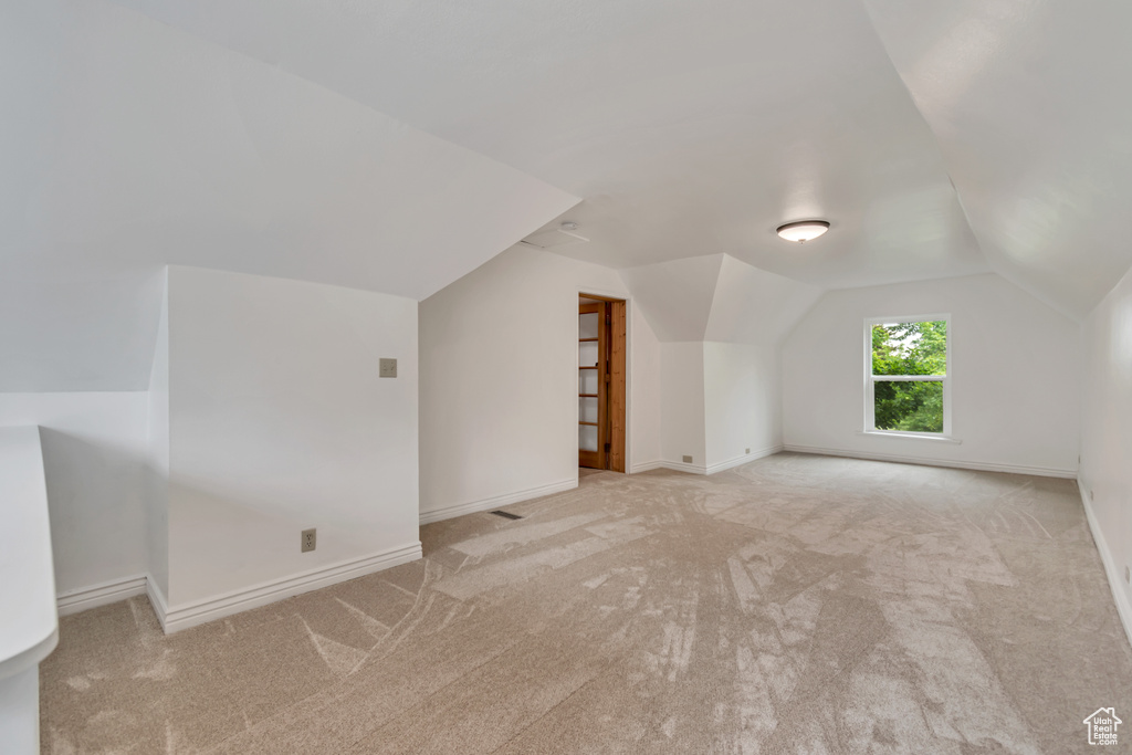Additional living space featuring light carpet, lofted ceiling, and baseboards
